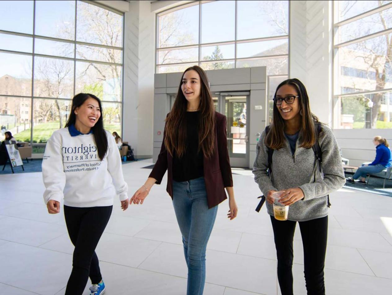 Three female Creighton students walking in Heider Business College entrance.